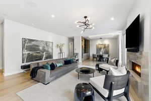 Living room with a fireplace, a chandelier, light wood-style flooring, and recessed lighting