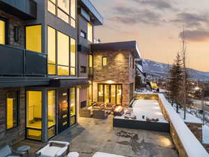 Snow covered back of property with stone siding, an outdoor hangout area, and a mountain view