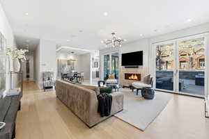 Living area featuring a lit fireplace, light wood finished floors, a chandelier, plenty of natural light, and recessed lighting