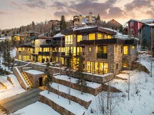 Snow covered rear of property featuring a balcony and stone siding