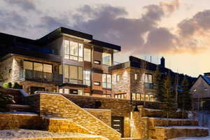 Snow covered property featuring a balcony, stone siding, and stucco siding