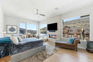 Bedroom featuring wood finished floors, multiple windows, a large fireplace, and a ceiling fan
