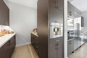 Kitchen featuring built in appliances, modern cabinets, light wood-style floors, and dark brown cabinetry