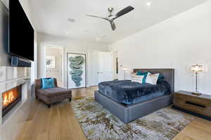 Bedroom with a tile fireplace, a ceiling fan, and light wood finished floors