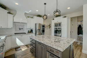 Kitchen with backsplash, a center island, white cabinets, light stone counters, and recessed lighting