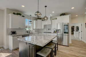 Kitchen with stainless steel appliances, light stone countertops, white cabinetry, a kitchen breakfast bar, and recessed lighting