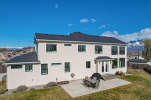 Back of house with a mountain view, a lawn, a patio, and roof with shingles