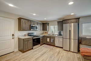 Kitchen featuring stainless steel appliances, light wood finished floors, recessed lighting, dark brown cabinetry, and light stone counters