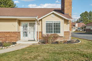 View of exterior entry featuring a lawn, brick siding, and a chimney