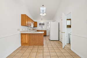 Kitchen featuring light countertops, a chandelier, brown cabinets, a peninsula, and decorative light fixtures