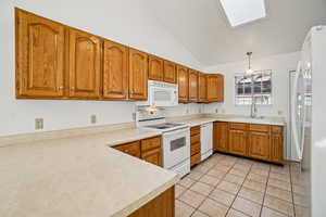 Kitchen with brown cabinets, white appliances, pendant lighting, light countertops, and lofted ceiling