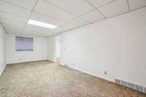 Carpeted empty room featuring a drop ceiling and baseboards