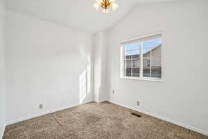 Carpeted empty room featuring lofted ceiling and a chandelier