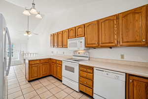 Kitchen featuring white appliances, brown cabinetry, light countertops, hanging light fixtures, and high vaulted ceiling