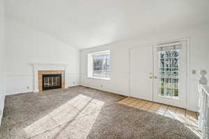 Unfurnished living room with a tiled fireplace, light colored carpet, lofted ceiling, and light tile patterned floors