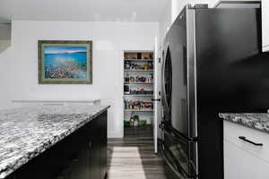 Kitchen with dark cabinets, light stone countertops, freestanding refrigerator, and dark wood-style floors