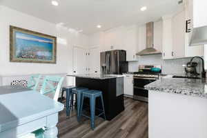 Kitchen with white cabinetry, wall chimney range hood, appliances with stainless steel finishes, light stone countertops, and recessed lighting