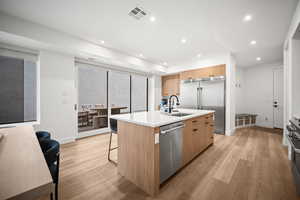 Kitchen with an island with sink, modern cabinets, light wood-type flooring, high end appliances, and recessed lighting