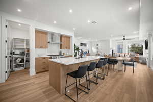 Kitchen featuring an island with sink, recessed lighting, wall chimney exhaust hood, a kitchen bar, and modern cabinets
