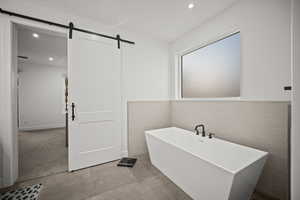 Full bath featuring recessed lighting, a soaking tub, and tile walls