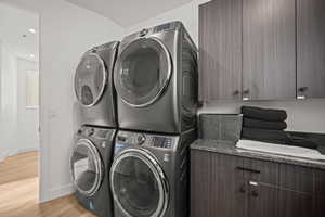 Laundry area featuring light wood-style floors, stacked washer and clothes dryer, and cabinet space