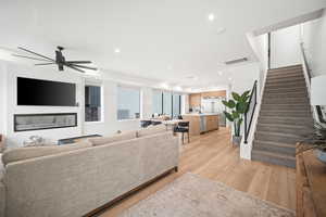 Living area featuring light wood-type flooring, stairway, recessed lighting, and a glass covered fireplace