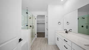 Bathroom with a stall shower, double vanity, a walk in closet, and recessed lighting