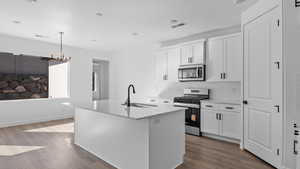Kitchen with stainless steel appliances, white cabinetry, a kitchen island with sink, dark wood-style flooring, and light stone countertops