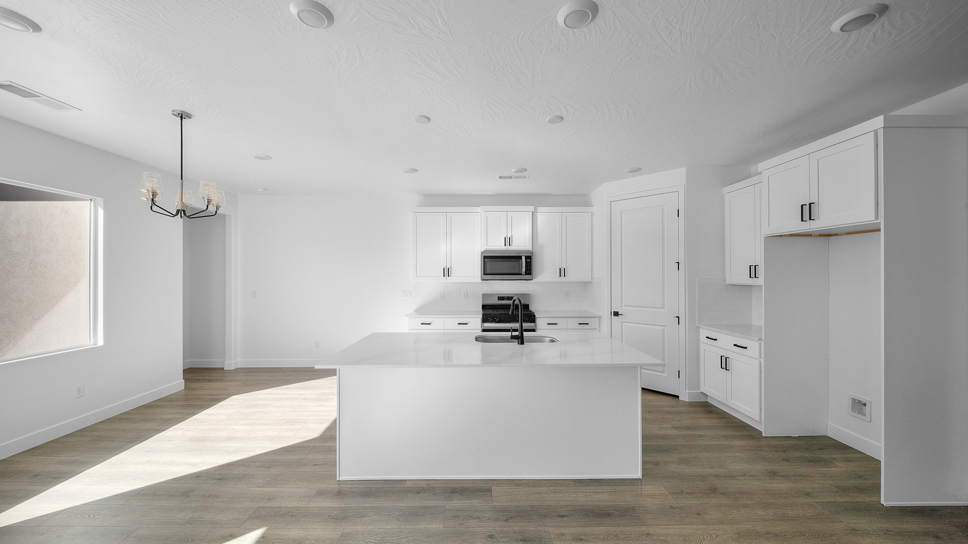 Kitchen with white cabinets, light stone counters, and a center island with sink