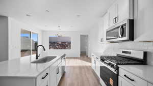 Kitchen with stainless steel appliances, light wood-style floors, a center island with sink, white cabinetry, and hanging lights