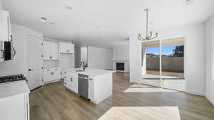 Kitchen featuring a large fireplace, an island with sink, white cabinetry, open floor plan, and light stone countertops
