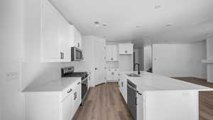 Kitchen with stainless steel appliances, white cabinetry, light wood finished floors, an island with sink, and light stone countertops