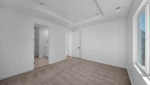 Unfurnished bedroom with light carpet, ensuite bath, and a raised ceiling