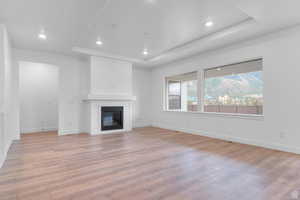 Unfurnished living room with a glass covered fireplace, a raised ceiling, light wood-style floors, and recessed lighting