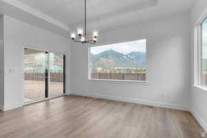Unfurnished dining area with a tray ceiling, a mountain view, a chandelier, and light wood-style flooring
