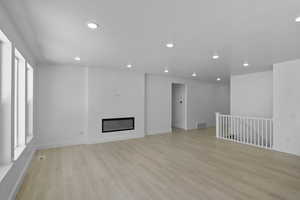 Unfurnished living room with light wood-style floors, recessed lighting, and a glass covered fireplace
