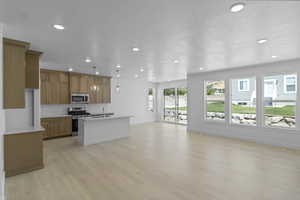 Kitchen featuring open floor plan, pendant lighting, stainless steel appliances, brown cabinetry, and an island with sink