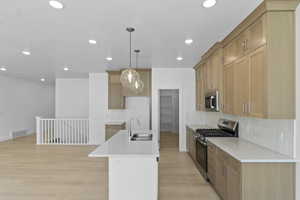 Kitchen featuring appliances with stainless steel finishes, decorative backsplash, pendant lighting, light stone countertops, and a center island with sink