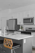Kitchen featuring white cabinetry, appliances with stainless steel finishes, light stone counters, and a kitchen bar
