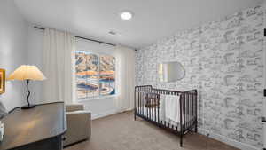 Carpeted bedroom featuring a crib and wallpapered walls