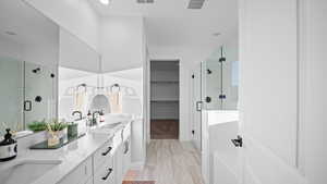Full bathroom featuring double vanity, a shower stall, a spacious closet, and light wood-style floors