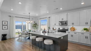 Kitchen featuring stainless steel appliances, light stone countertops, an island with sink, hanging lights, and dark wood-type flooring