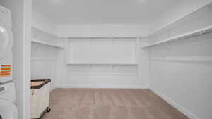 Walk in closet featuring light colored carpet and stacked washer / dryer