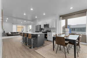Kitchen with open floor plan, an island with sink, stainless steel appliances, white cabinetry, and a kitchen breakfast bar