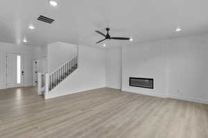 Unfurnished living room with stairs, a glass covered fireplace, recessed lighting, light wood-style floors, and ceiling fan