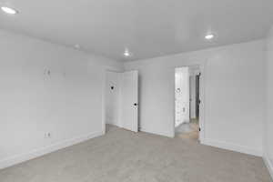 Unfurnished bedroom with light colored carpet, recessed lighting, and ensuite bathroom