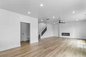 Unfurnished living room with a glass covered fireplace, stairs, light wood-style floors, recessed lighting, and ceiling fan