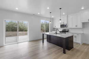 Kitchen with white cabinets, dark brown cabinetry, appliances with stainless steel finishes, a center island with sink, and light stone countertops