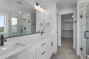 Bathroom with a marble finish shower, a spacious closet, double vanity, and light tile patterned floors