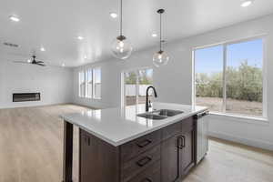 Kitchen featuring dark brown cabinetry, light wood finished floors, light stone counters, hanging light fixtures, and recessed lighting